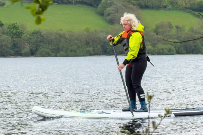 Kay paddleboarding in technical paddle clothing and water shoes on a UK lake