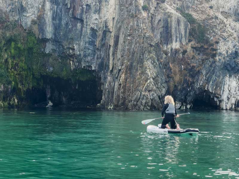 Explore paddleboarding locations — a paddler beside coastal cliffs