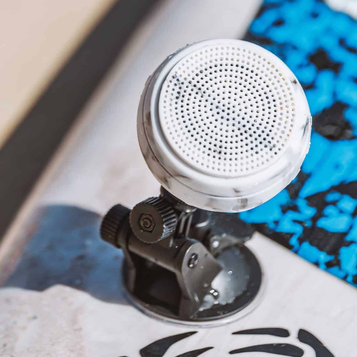 Front close-up of a white speaker on a Speaqua Board Mount beside a blue paddle board deck pad