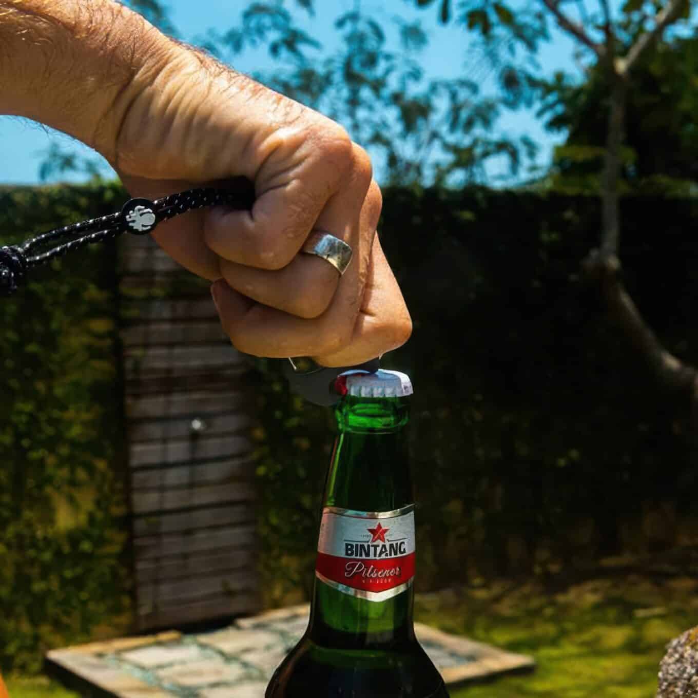 Hand using the Speaqua carabiner clip’s built-in bottle opener to open a bottle outdoors