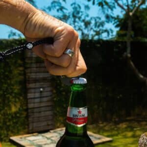 Hand using the Speaqua carabiner clip’s built-in bottle opener to open a bottle outdoors