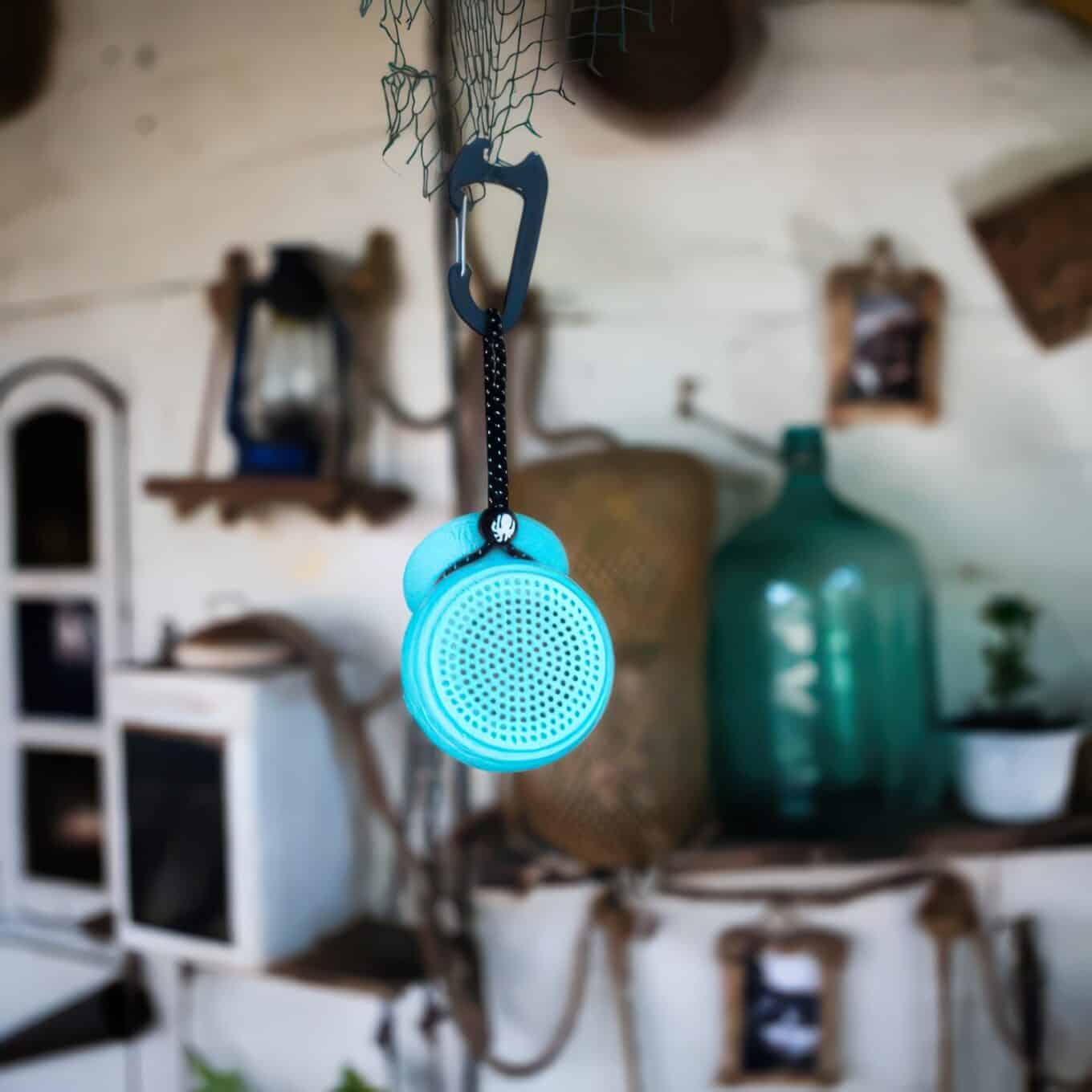 Speaqua Barnacle Pro speaker suspended indoors from a carabiner clip and leash cord attached to netting