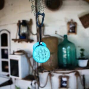 Speaqua Barnacle Pro speaker suspended indoors from a carabiner clip and leash cord attached to netting